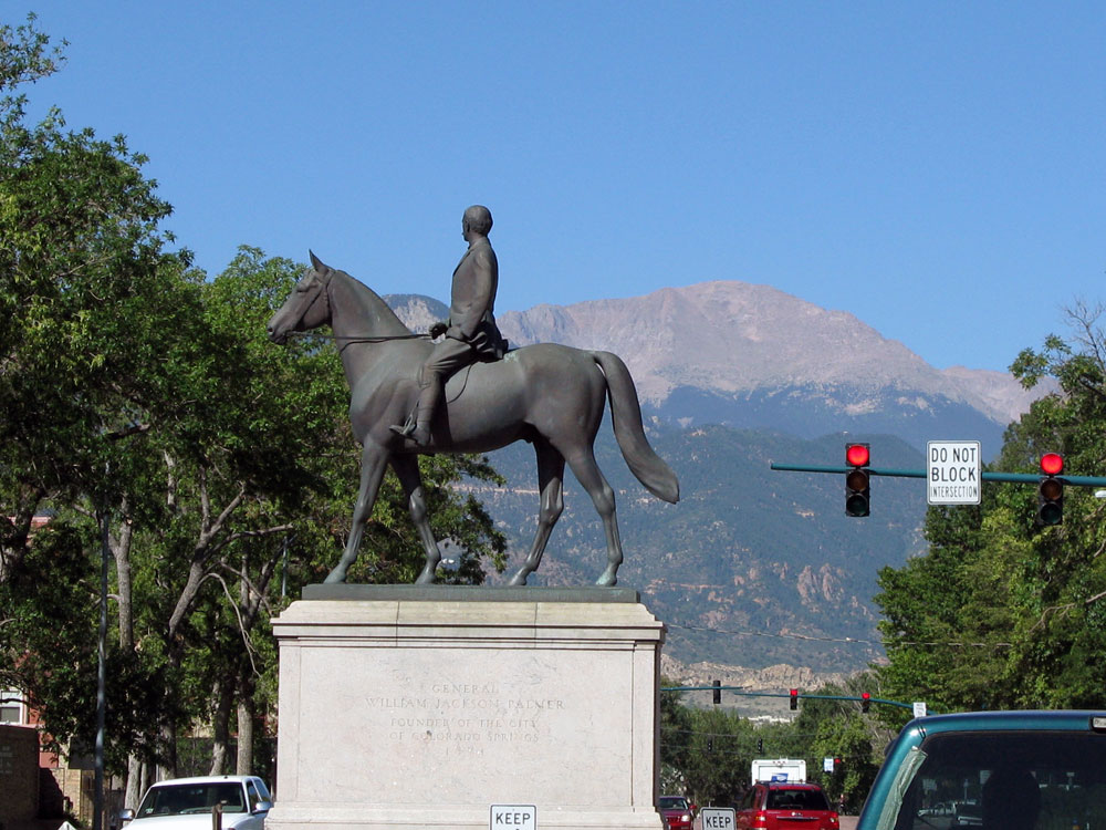 A statue of General William Jackson Palmer astride a horse faces Pikes Peak. There are traffic lights with "Do Not Block Intersection" signs atop the poles. 