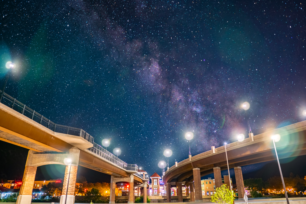 A bridge lit up at night with a starry night sky above it