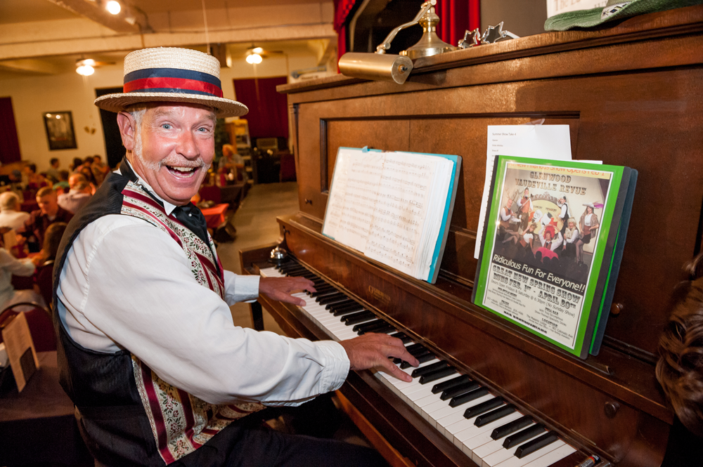 A man in a vaudeville costume smiles while playing the piano