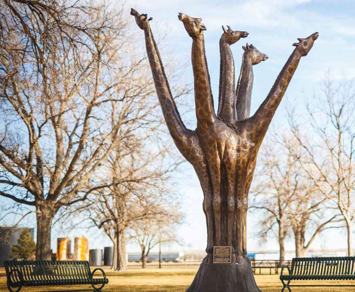Five giraffe bodies come out of a base reaching toward the light-blue sky.