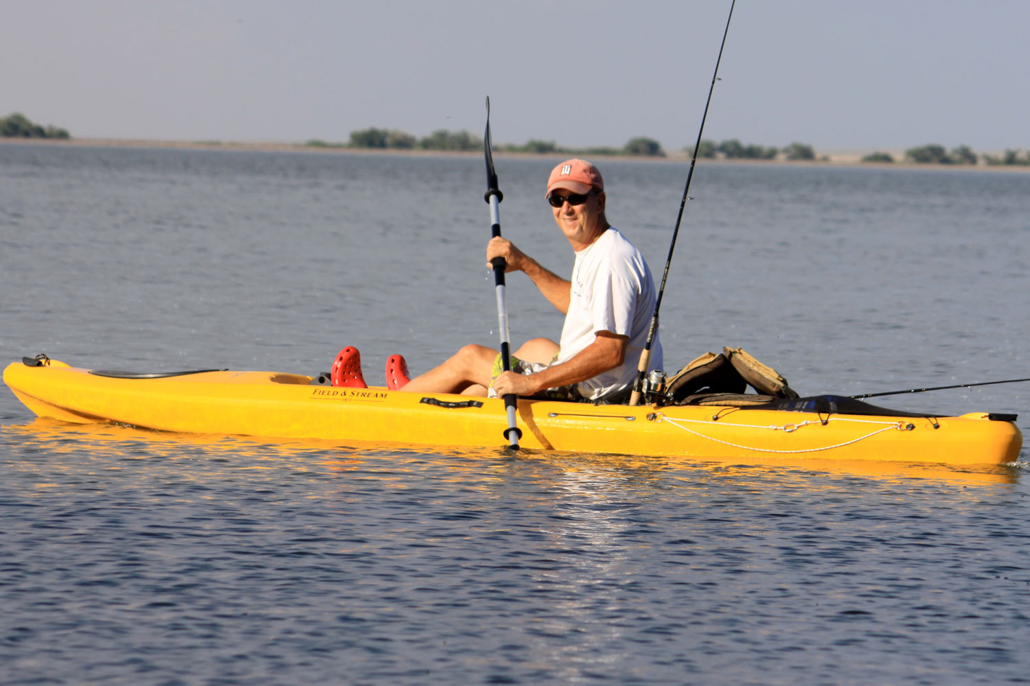 A person sits in a yellow kayak smiling at the camera on rippling water. 