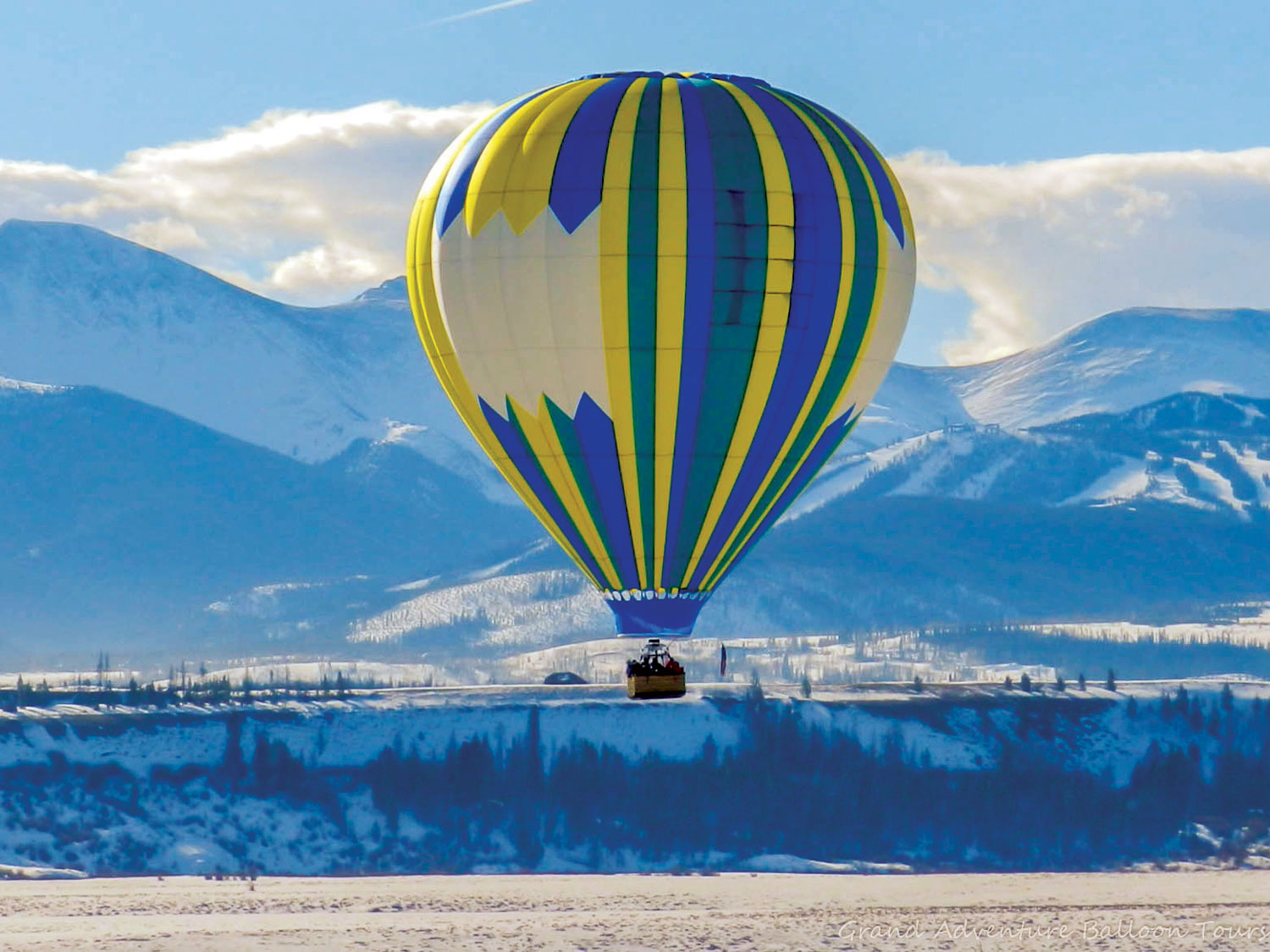 A colorful hot air balloon floats along with snowy mountains behind it