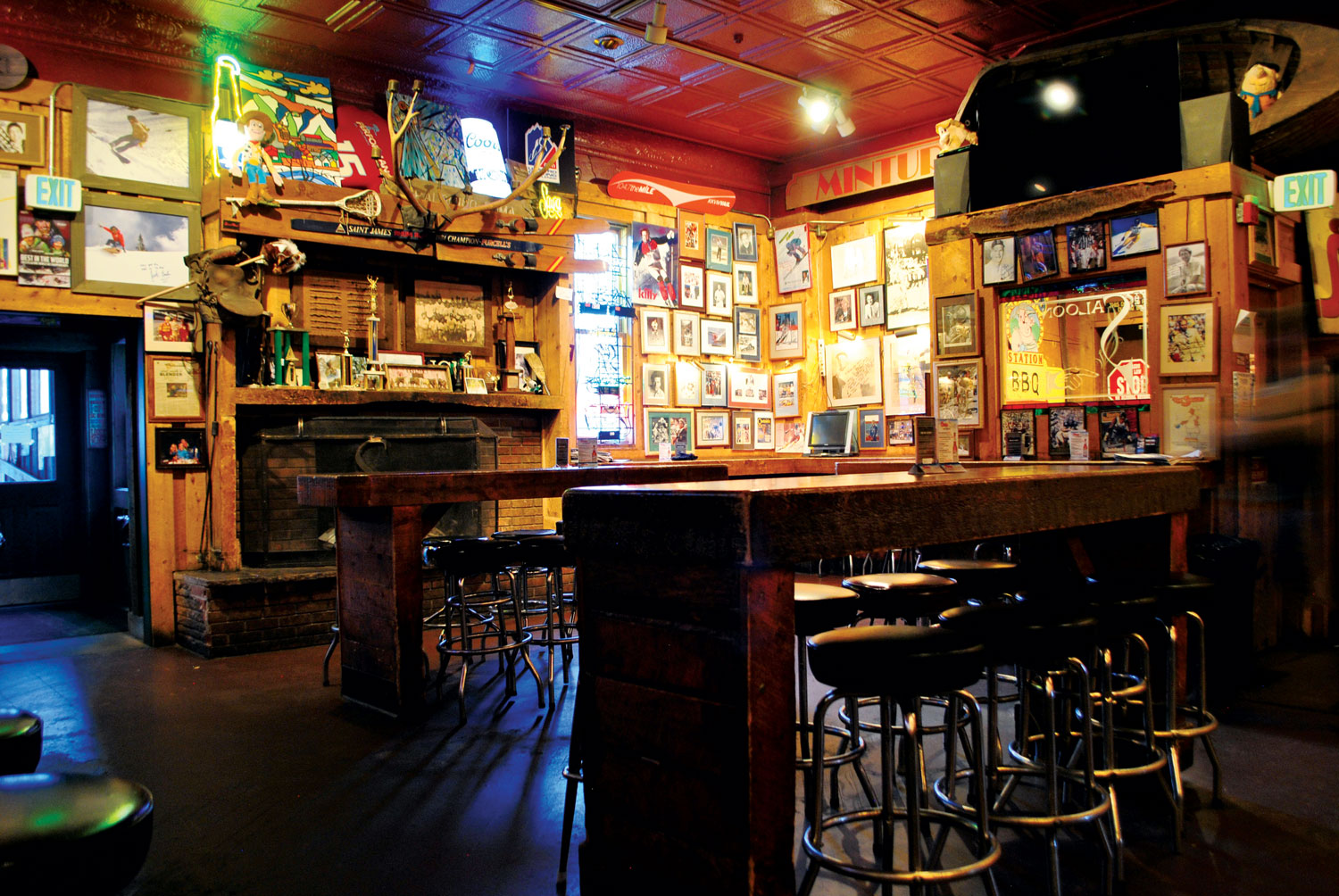 Framed photos crowd the wood-paneled walls of the Minturn Saloon in Minturn, Colorado. Two narrow, bar-style tables run through the space with cushioned bar stools lined up below.