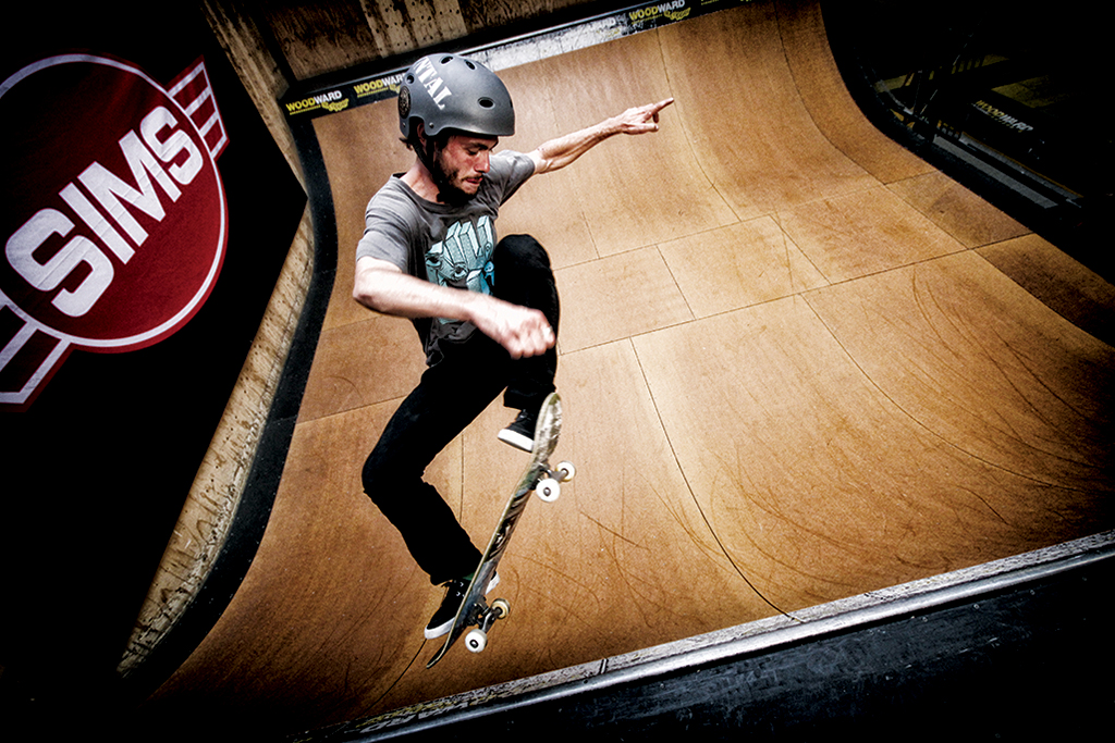 A skateboarder on an indoor half pipe ollies into the air