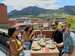 Eat Happy in Boulder A group of four people eating on a rooftop in Boulder with the Flatirons in the background