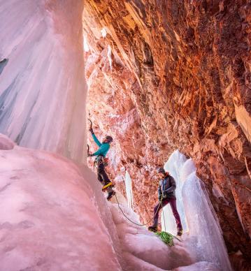 A couple scales a wall of ice in a red-rock canyon