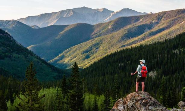 A man stands on a rock outcropping gazing at a mountainous horizon