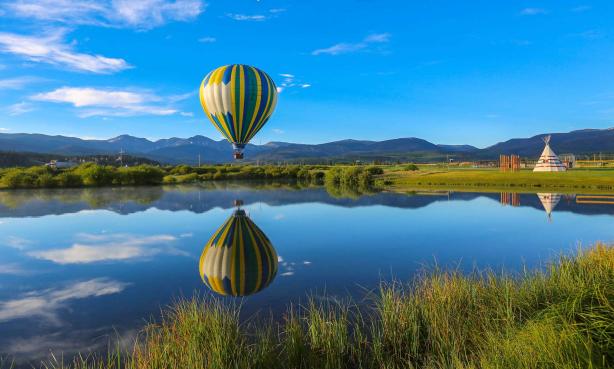 Hot-air balloon reflected in still waters with mountains in the background near Winter Park