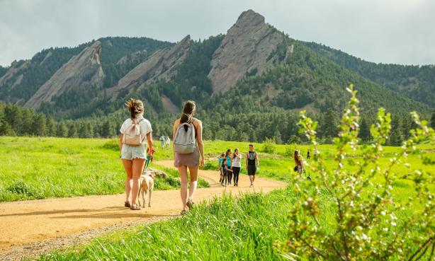 Boulder Flatirons in summer with two women walking a dog in the foreground.