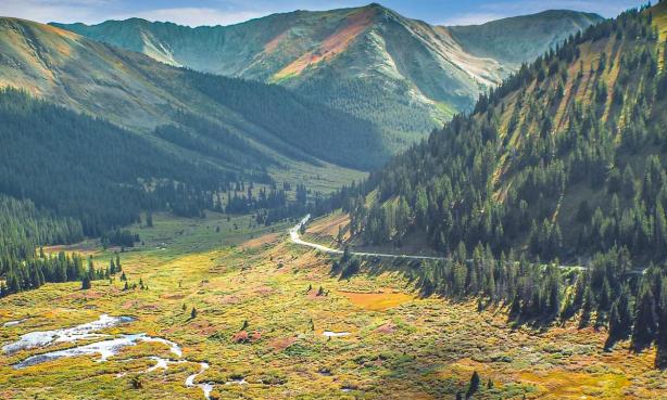 A meandering road cuts through sunlight-dappled mountain scenery near Leadville and Twin Lakes.