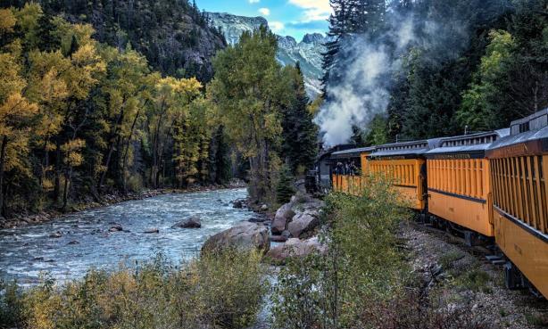 The Durango Train runs alongside a river in a canyon where the trees are just turning gold for autumn