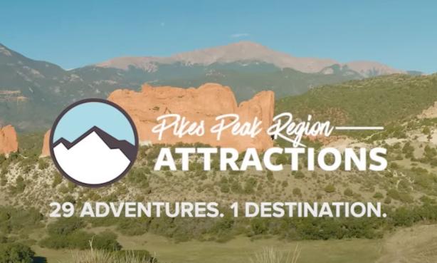 White text that says "Pikes Peak Region Attractions" and "29 Adventures, 1 Destination." Beside the text is a circular logo with a drawing of white mountains beneath blue sky. Behind the text and logo is a scenic photograph of a vast hilly plain dotted with dark green bushes and grass. Behind the plain are two large tan rocky structures jutting out from the ground. Behind those presumably miles and miles away is Pikes Peak, a tall purple-blue mountain structure. The sky above is dusty blue.