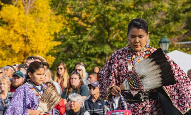 A Native American woman and girl perform a dance at Elk Fest in Estes Park while holding feathered fans while a crowd watches