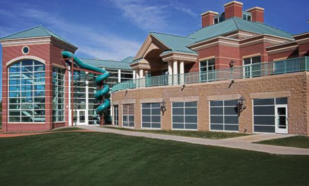 A twisting, forest-green slide outside the welcome center buildings, with a sprawling green lawn in front