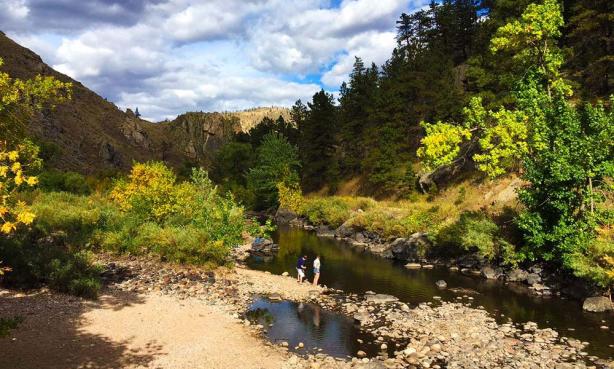 Two people stand on the rocky banks of the Cache la Poudre River at Gateway Natural Area in Fort Collins, Colorado