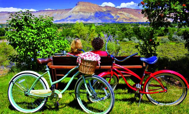 Two people sit on a bench with two bikes leaning on it, looking at a mountain