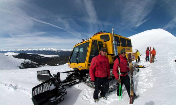 Group of skiers standing by a snowcat on a mountain top