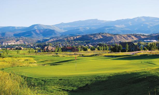 The rolling green course of Eagle Ranch Golf Course sits peacefully beneath distant, majestic, blue-and-purple mountains.