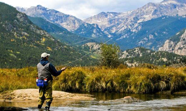 A man stream fishing in Rocky Mountain National Park with fall colors and mountain peaks rising in the distance