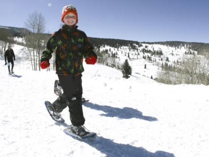 A young man showshoes under a bright blue ski - Beaver Creek, CO