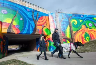 Man and girl walk a dog past a colorful mural