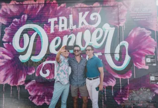 Men pose before a Talk Denver to Me mural in Denver's RiNo neighborhood