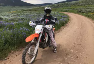 Person rides a dirt bike on a trail through the mountains