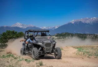 People riding in an ATV with snowcapped mountains in the background