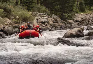 Red inflatable boat with three people whitewater rafting through rapids.