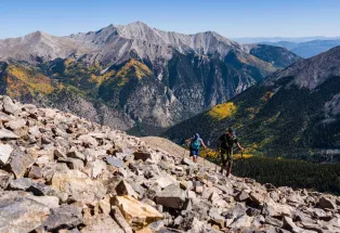 Two hikers navigate a rock field on a fourteener with majestic peaks in the background