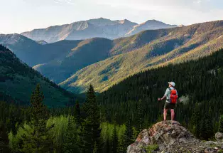 A man stands on a rock outcropping gazing at a mountainous horizon