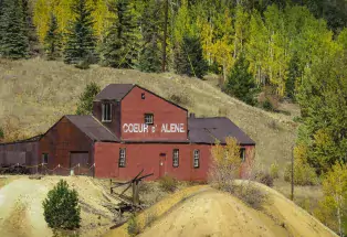 Coeur d' Alene Mine, a red barn-like building at the beginning of fall with green trees turning golden in the background.