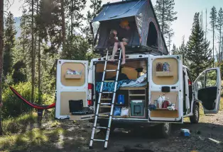 Parent and child relax in a tent on the roof of a campervan. 