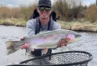 A man poses with an opalescent trout with a fishing net below on the Arkansas River near Leadville.