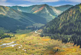 A meandering road cuts through sunlight-dappled mountain scenery near Leadville and Twin Lakes.