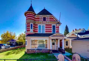 A colorfully painted Victorian home with turrets stands tall against a bright bluebird sky.