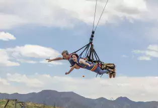 Two kids lying on their stomachs with their arms out on the Royal Rush Skycoaster, suspended above the mountain range in the background. 