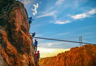 Four people climbing the Via Ferrata with the Royal Gorge Bridge in the background.