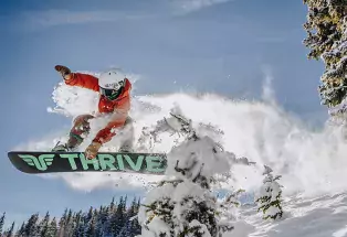 Snowboarder flying off a jump with snow trailing behind him