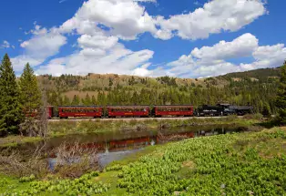 A mountain pasture with a pond and train the background.