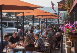 People eating at outdoor cafe tables with umbrellas at Sagebrush BBQ & Grill along the Grand Lake Boardwalk