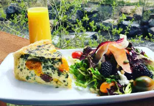 A vegetable quiche, colorful salad with berries and melon, and a glass of orange juice overlooking the waters of Clear Creek