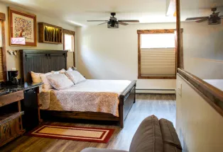 A cozy historical hotel room in Georgetown, Colorado with a ceiling fan, hardwood floors and a dark wooden bed frame.
