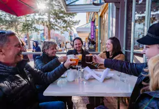 A group of friends toasting each other with mugs of hot cider and tea on an outdoor patio in Boulder Colorado.