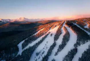 An aerial view of the runs at Eldora Ski Area — fat streaks of white snow among thick fir forests with the snow-covered Rocky Mountains in the background
