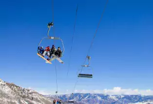 Snowboarders and skiers ride a chairlift at Snowmass Mountain with a vast bluebird blue sky behind them