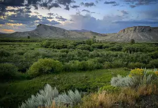 Ridged cliffs with green grass and shrubs in the foreground near Kremmling