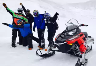 Snowmobilers with High Country Tours pause by their snowmobile with arms in the air near Kremmling
