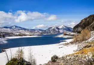 Green Mountain Reservoir near Kremmling is half frozen and covered in snow with mountains and a bright-blue sky with puffy white clouds in the background