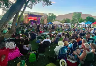 A crowd of people sitting on a lawn face a stage at the Palisade Bluegrass Festival